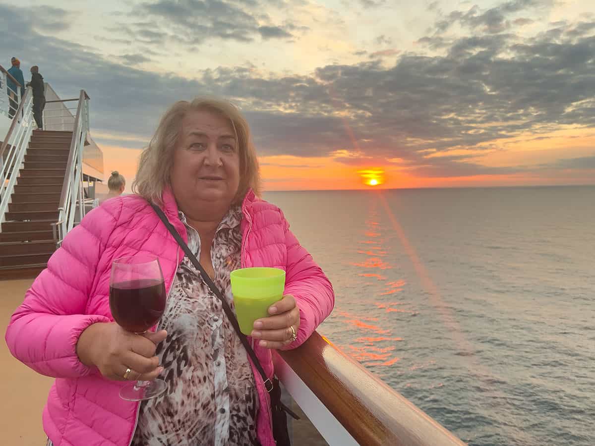 Morag on ships deck at night with a drink in both hands